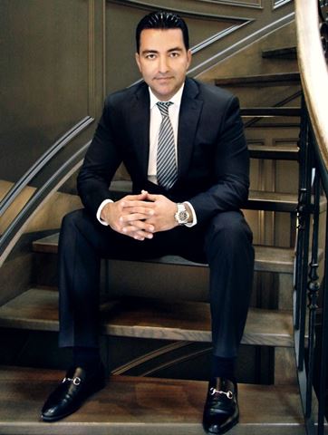 Mark Aliassa seated on stairs in a dark suit